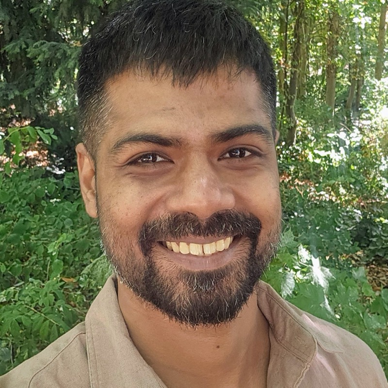 Govind Ravi Sulekha, head and shoulders, smiling, in a linen shirt with trees behind